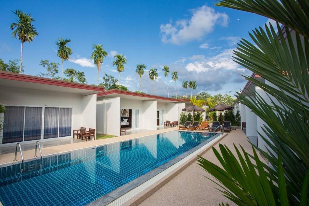 a swimming pool in front of a house with palm trees at Baan Chong Fa Resort in Khao Lak