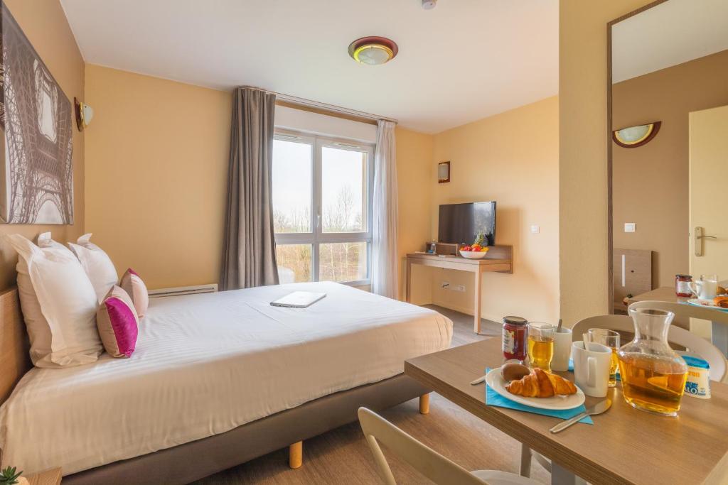 una habitación de hotel con una cama y una mesa con comida. en Zenitude Hôtel-Résidences Magny-les-Hameaux, en Magny-les-Hameaux
