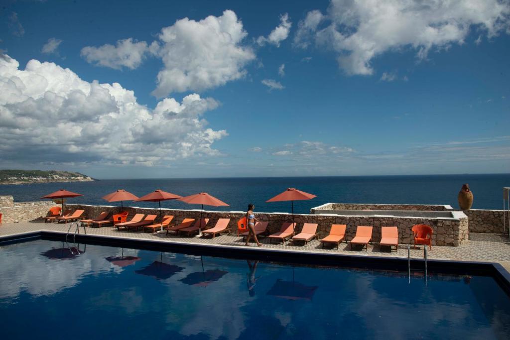 a swimming pool with chairs and umbrellas and the ocean at Hotel Piccolo Mondo in Castro di Lecce