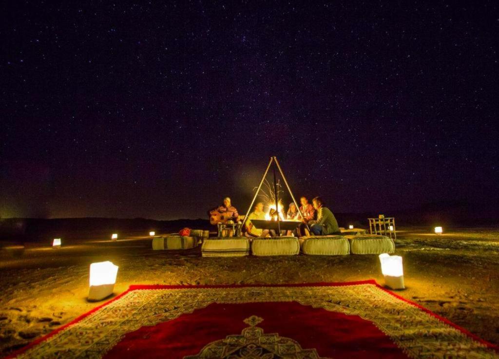 Eine Gruppe von Menschen, die nachts um ein Feuer herum sitzen in der Unterkunft Chigaga Desert Camp in M’hamid El Ghizlane