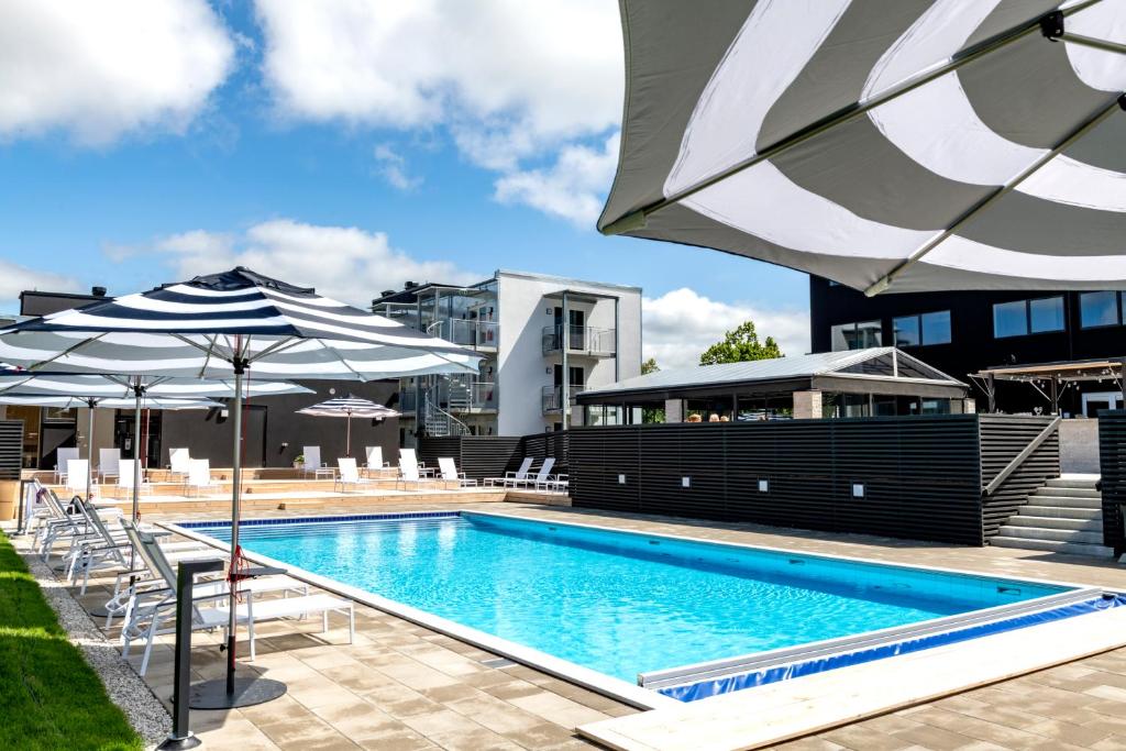 a swimming pool with chairs and umbrellas next to a building at First Hotel Kokoloko in Visby