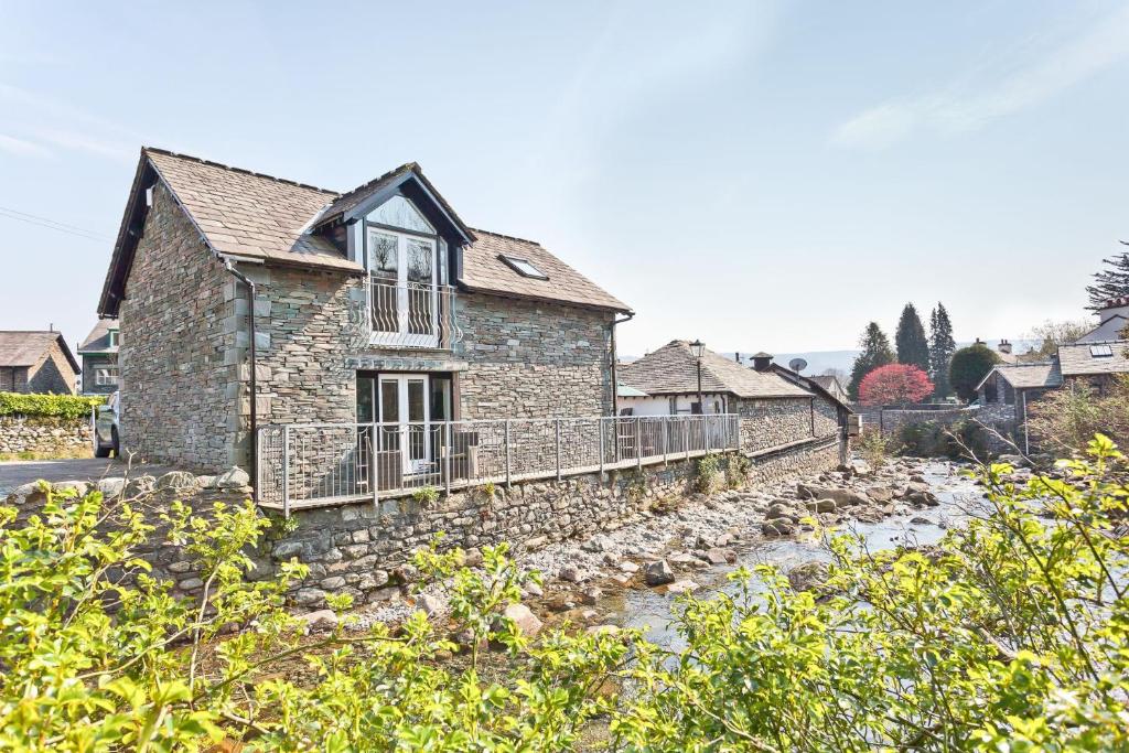 a stone house with a stone wall next to a river at Forge Bridge Cottage Coniston in Coniston