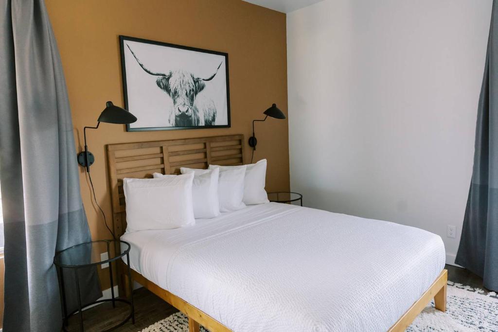 a bed with white pillows and a picture of a cow at Unit 222 - The Lyndon 1 Bed - Cation on the Guadalupe in New Braunfels