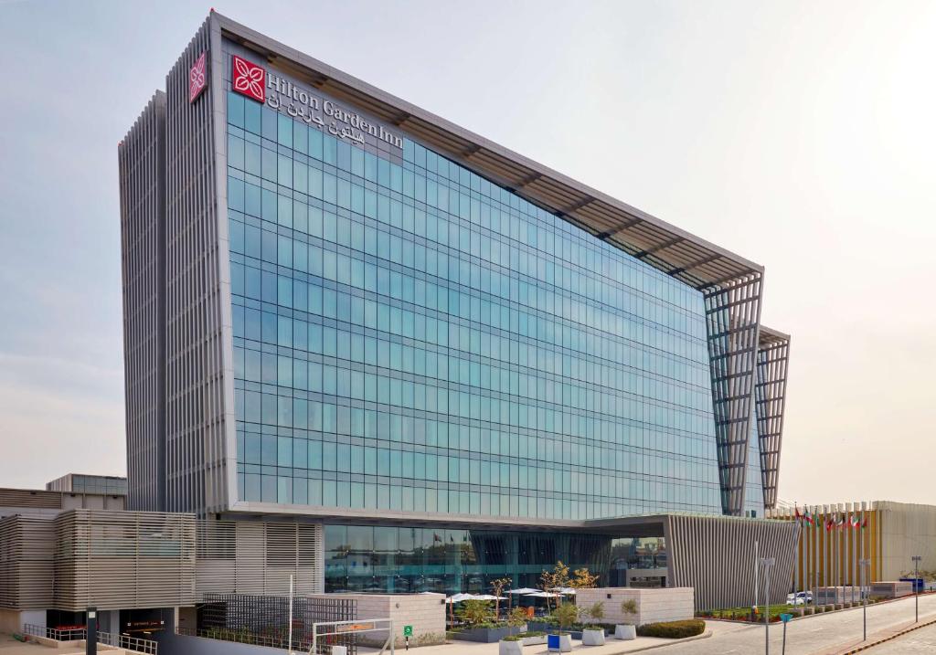 a tall glass building with a sign on it at Hilton Garden Inn Kuwait in Kuwait