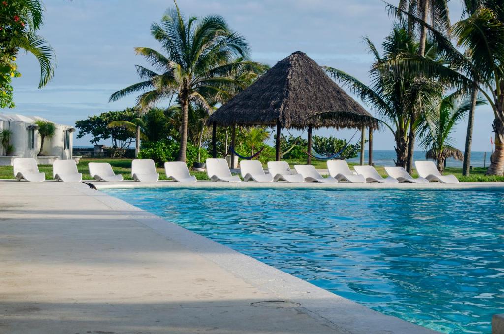 - une piscine avec des chaises longues blanches et un parasol dans l'établissement Hotel Boca de Ovejas, à El Morro