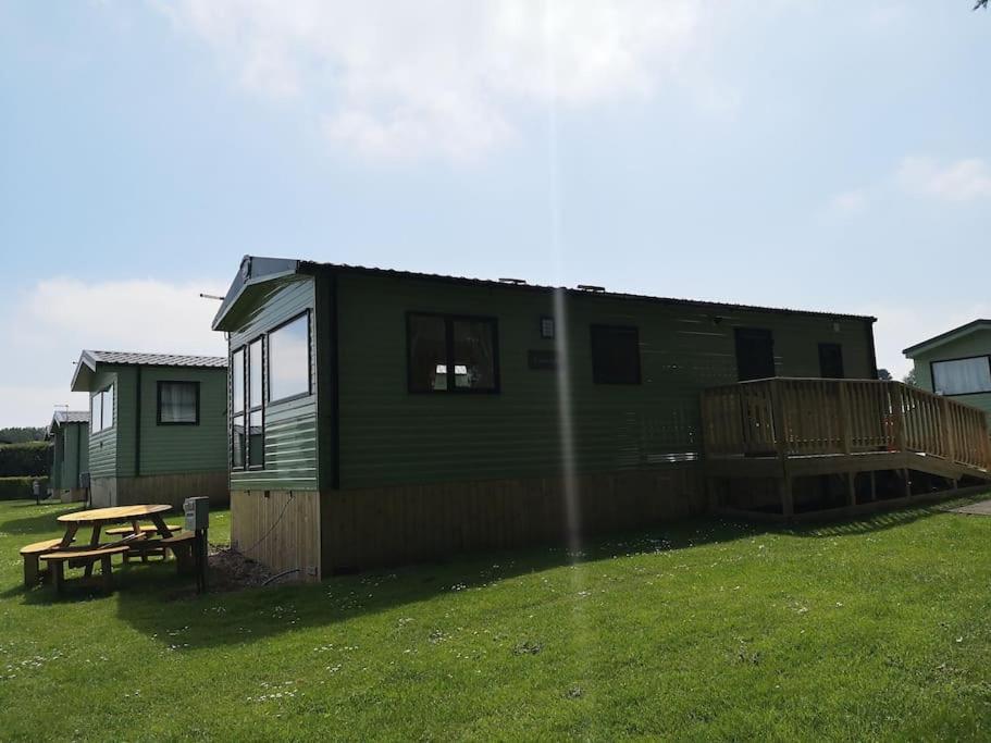 una casa verde con una mesa de picnic en un patio en Plompton Mill Holiday Home, en Knaresborough