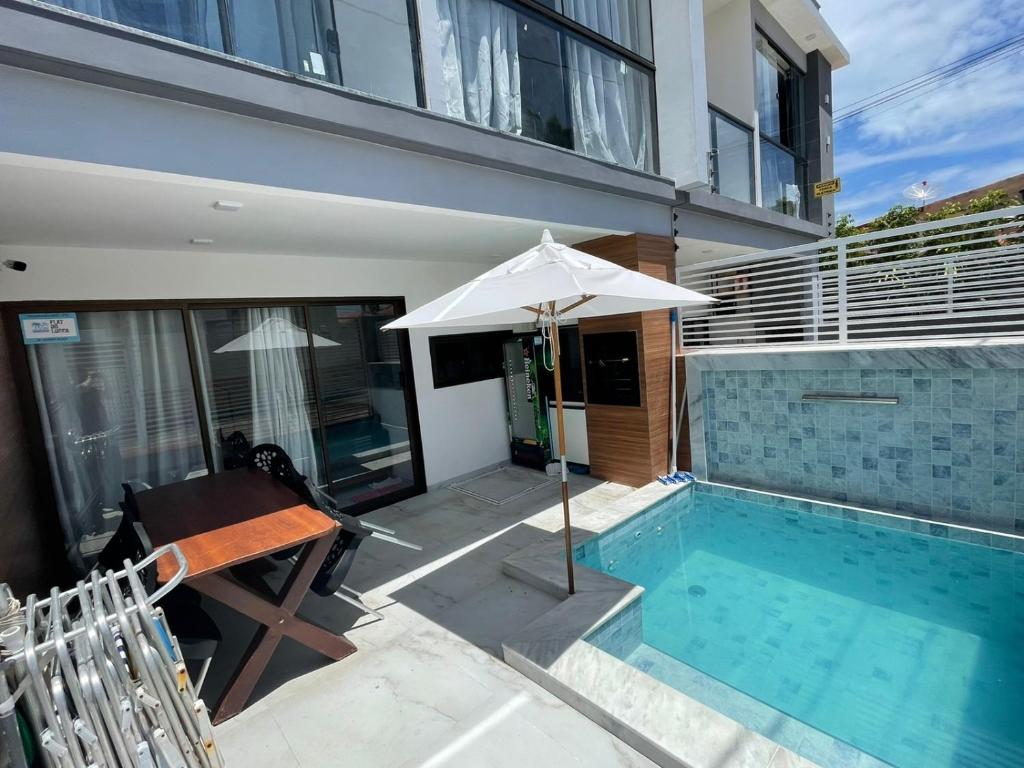 a swimming pool with an umbrella next to a house at Flats do Lucca in Tamandaré