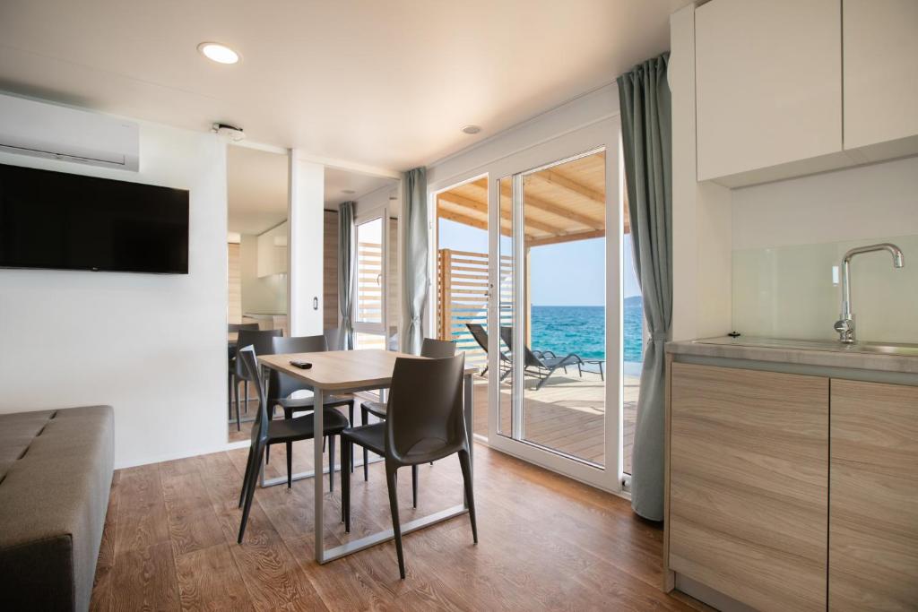 eine Küche und ein Esszimmer mit einem Tisch, Stühlen und Meerblick in der Unterkunft Deluxe Beach Mobile Homes in Šibenik