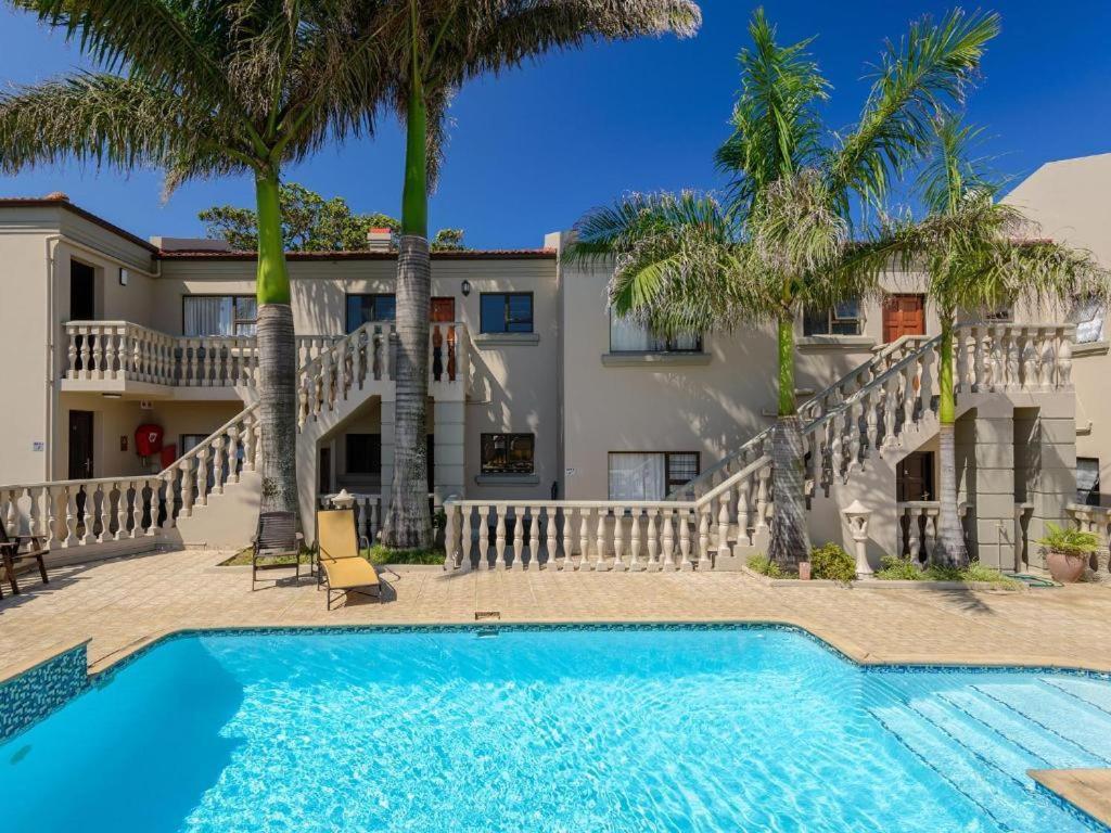 a swimming pool in front of a house with palm trees at Pebble Beach in Uvongo Beach