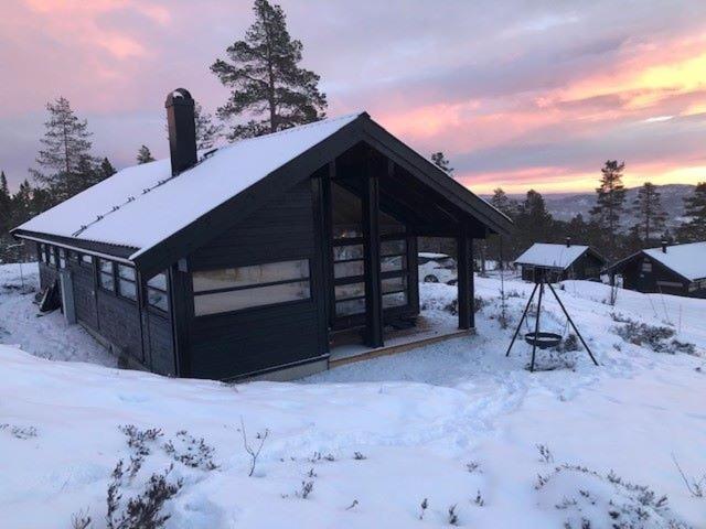 a cabin with a snow covered roof in a field at Myrullen - Cabin at Sørbølfjellet in Flå
