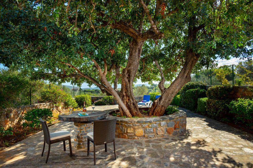 a patio with two chairs and a table under a tree at Carob Cottage in Elounda
