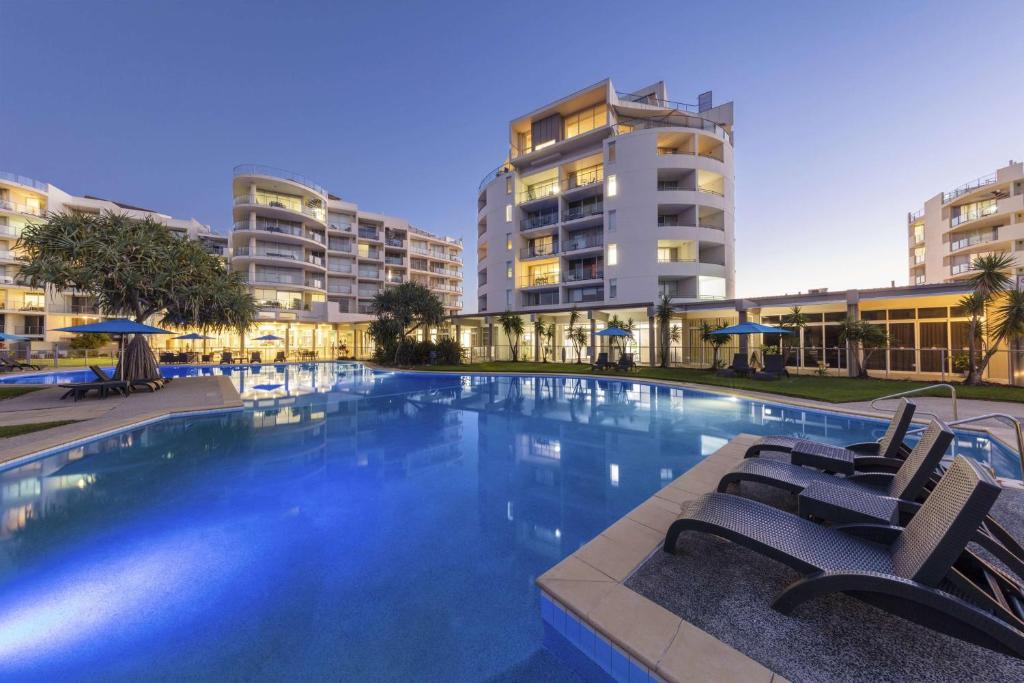 a large swimming pool with chairs and buildings at Ramada By Wyndham Marcoola Beach in Marcoola