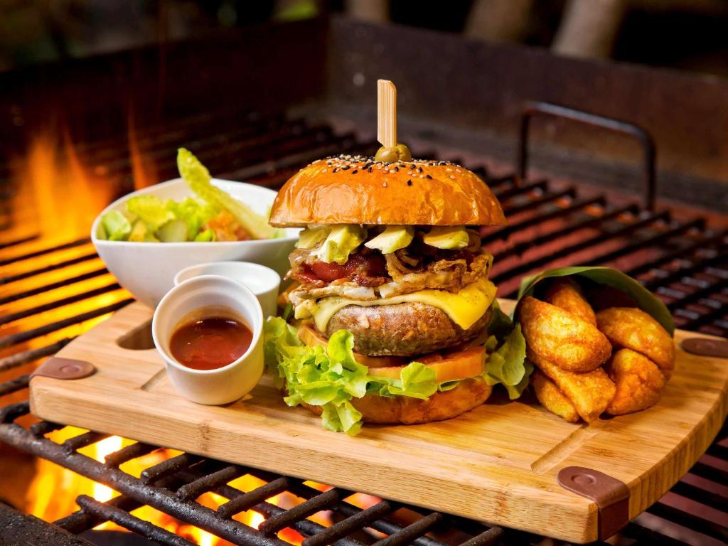 a hamburger on a cutting board with a salad and dipping sauce at Hotel Ibis Samui Bophut in Bophut