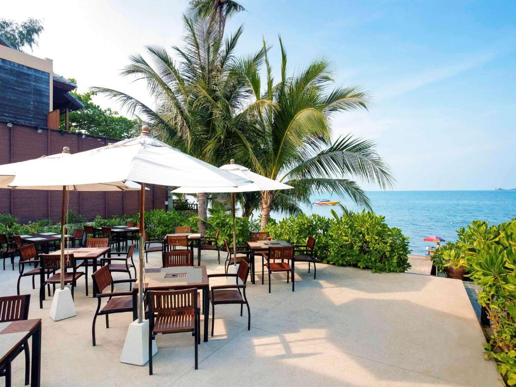 an outdoor restaurant with tables and chairs and the ocean at Hotel Ibis Samui Bophut in Bophut