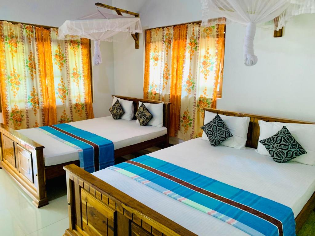 two beds in a room with orange curtains at Rich Resort & Restaurant in Anuradhapura