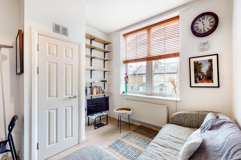een woonkamer met een bank en een klok aan een muur bij Charming 1 bedroom flat with parking in Brentford in Brentford