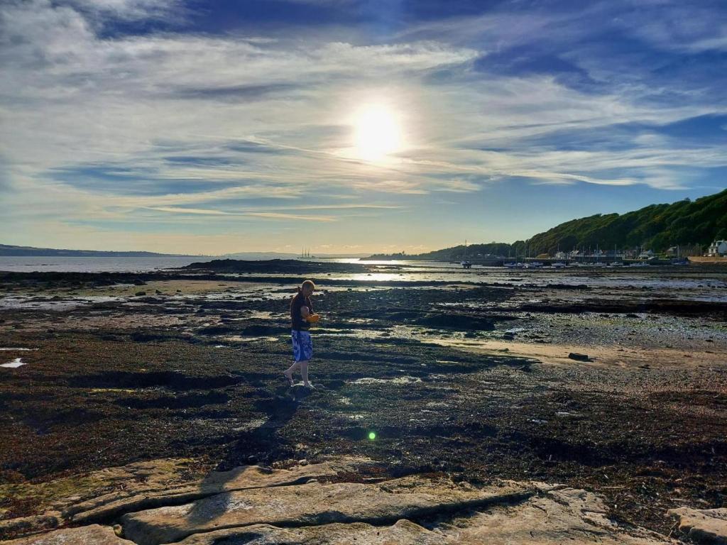 a person standing on a beach near the water at Lovely 2BD Flat in picturesque Limekilns Fife in Limekilns
