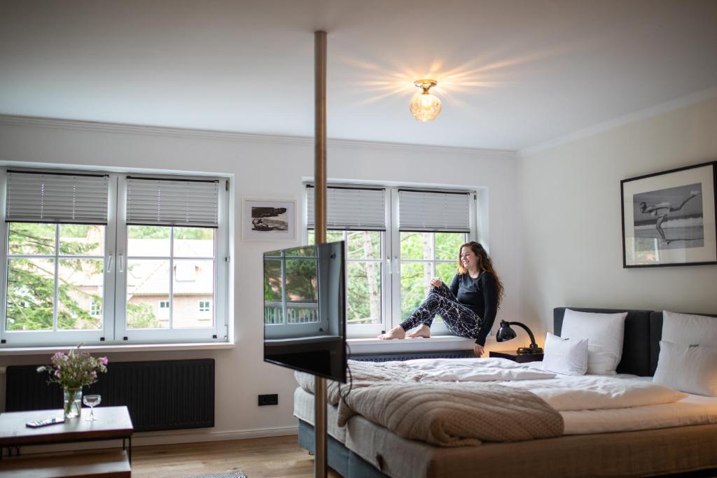 una mujer sentada en una cama en una habitación con ventanas en Das Kubatzki, en Sankt Peter-Ording