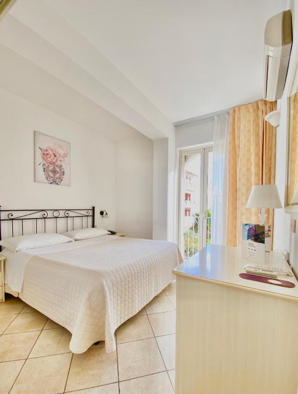 a white bedroom with a bed and a desk at Hotel Sylesia in Letojanni