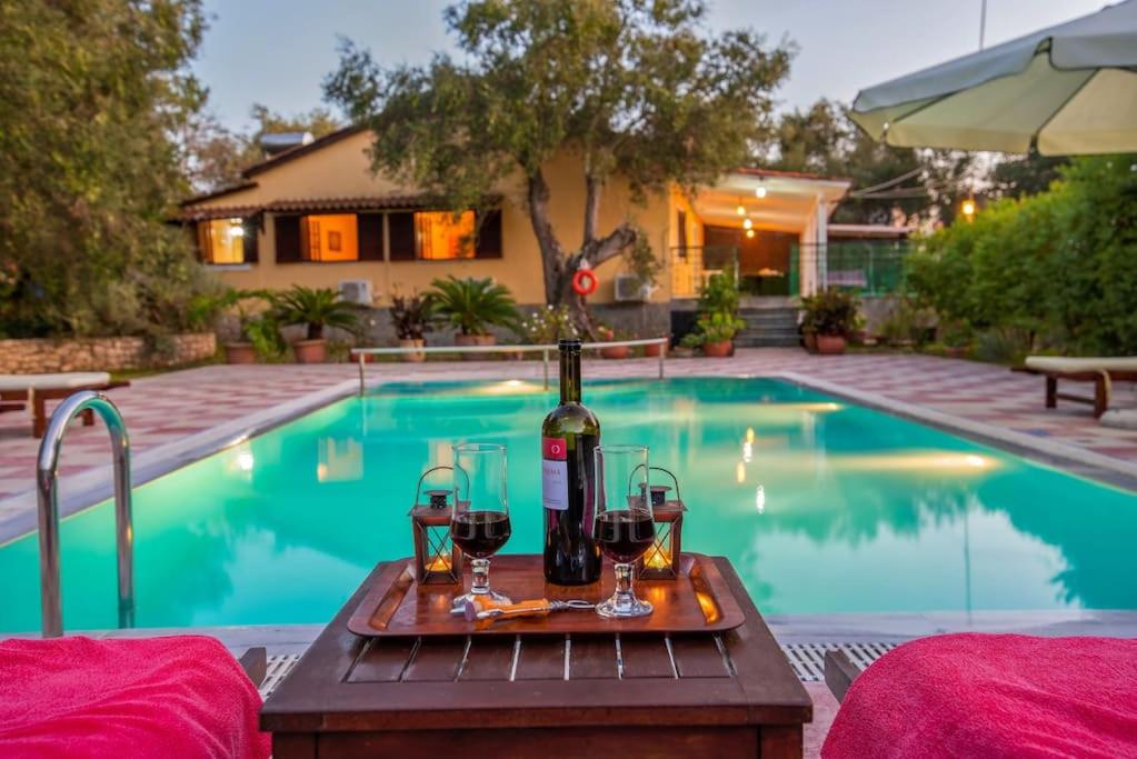 a table with a bottle of wine and glasses next to a swimming pool at Olive Tree Villa in Ieromónachos