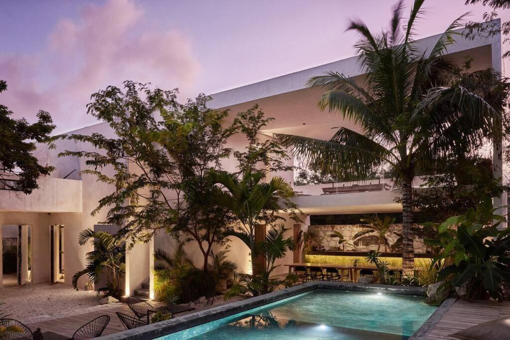 a swimming pool in front of a building with trees at Villa 16Tulum in Tulum