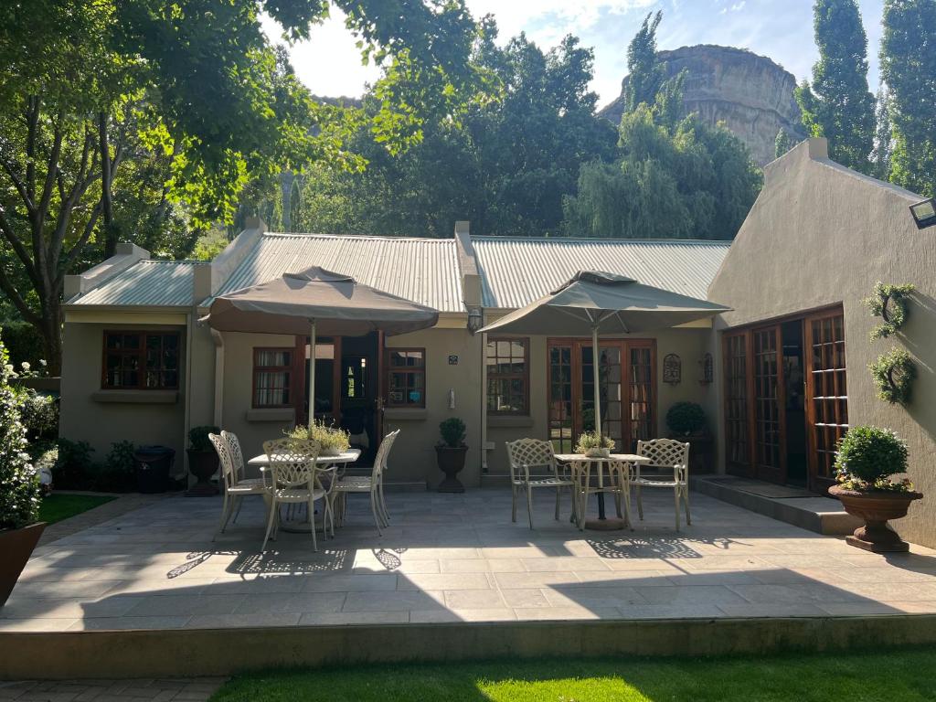 a patio with tables and umbrellas in front of a house at Zwartmodder Clarens in Clarens