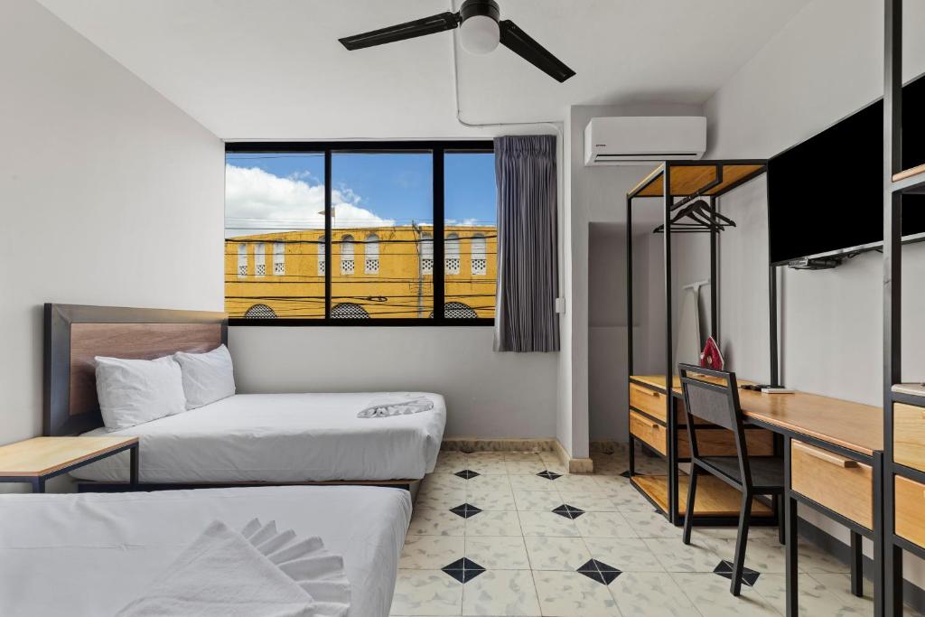 a room with two beds and a desk and a yellow building at Suites Reforma by HomiRent in Mérida