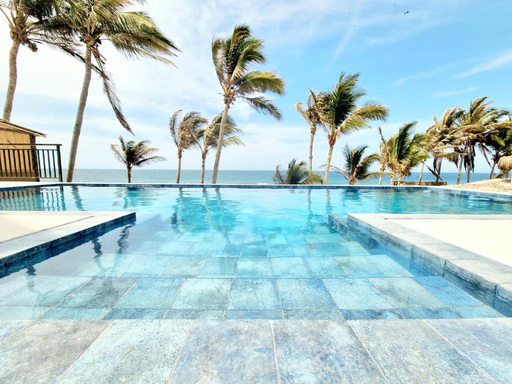 a swimming pool with palm trees and the ocean at Condominio, Las Pocitas de Máncora- Deluxe in Máncora