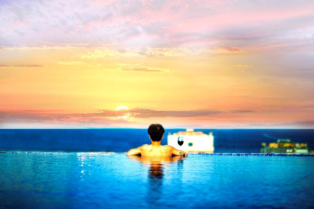 Ein Mann sitzt in einem Infinity-Pool und sieht den Sonnenuntergang. in der Unterkunft FIVITEL King in Đà Nẵng