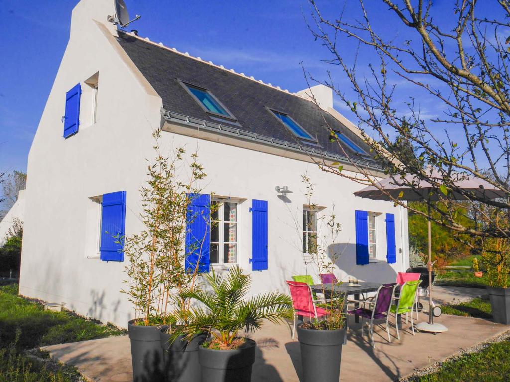 Biały dom z niebieskimi okiennicami oraz stołem i krzesłami w obiekcie Maison Neuve Confortable Proche Plages à Locmaria – Jardin, Terrasse, Wifi, Classée 3* - FR-1-418-209 w mieście Locmaria