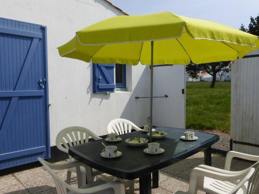 une table noire avec un parasol et des chaises jaunes dans l'établissement Maison 2 pièces/mezzanine, piscines chauffée, tennis - Bretignolles-sur-Mer - FR-1-224A-666, à Bretignolles-sur-Mer