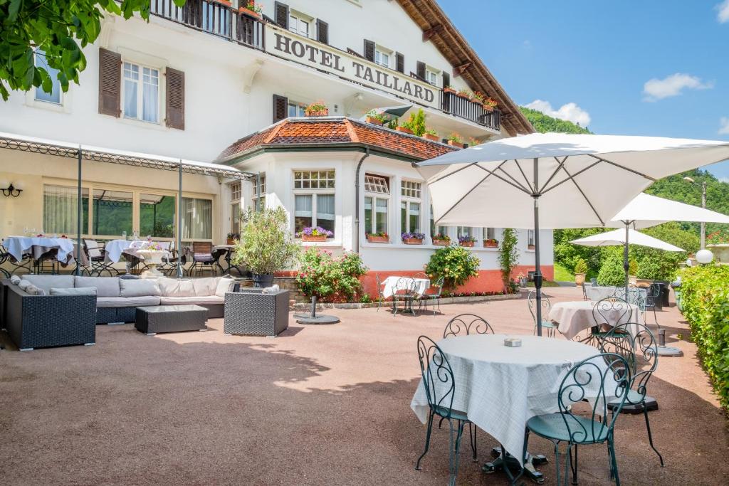 ein Hotel mit einem Tisch, Stühlen und einem Sonnenschirm in der Unterkunft Hôtel Restaurant Taillard in Goumois