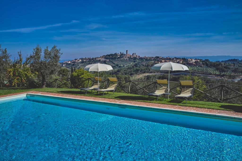 a swimming pool with chairs and umbrellas on a hill at Podere Sant'Elena in San Gimignano
