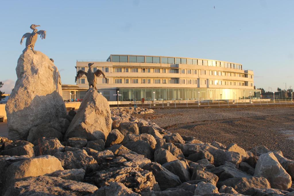 two birds on rocks on a beach with a building at The Midland in Morecambe
