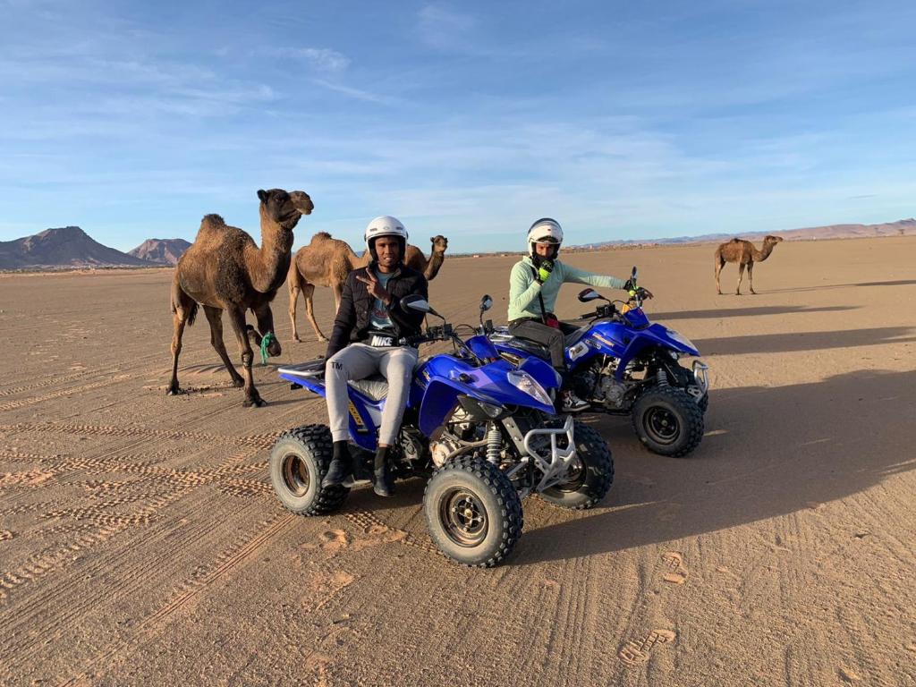 Zwei Menschen auf ATvs und ein Kamel in der Wüste in der Unterkunft Bivouac Draa in Zagora