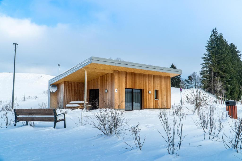 un edificio de madera con un banco en la nieve en Ô Doubs Chalets, en Mouthe