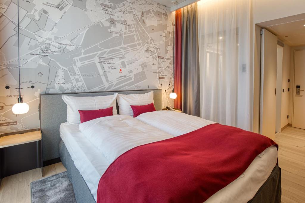 a bedroom with a large bed with red and white sheets at IntercityHotel Berlin Airport BER Terminal 1 & 2 in Schönefeld