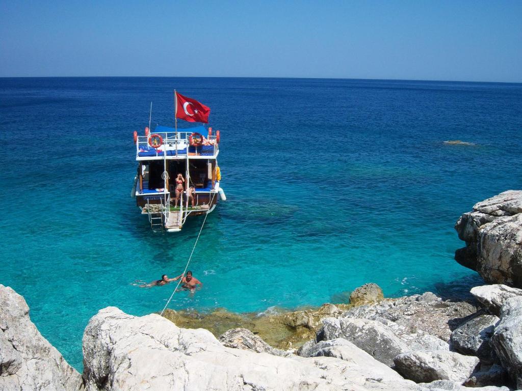 a boat with a flag and people in the water at Papirus Hotel in Adrasan