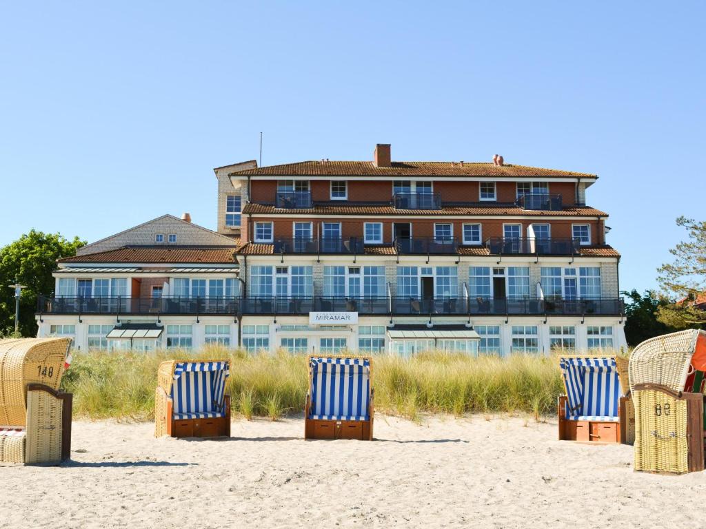 un gruppo di sedie in spiaggia con un edificio di Strandhotel Miramar a Timmendorfer Strand