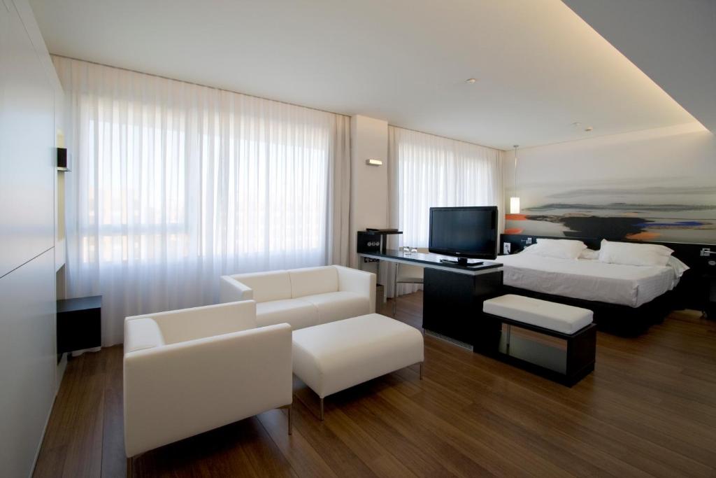 a living room with white furniture and a bed and a television at Axor Barajas in Madrid
