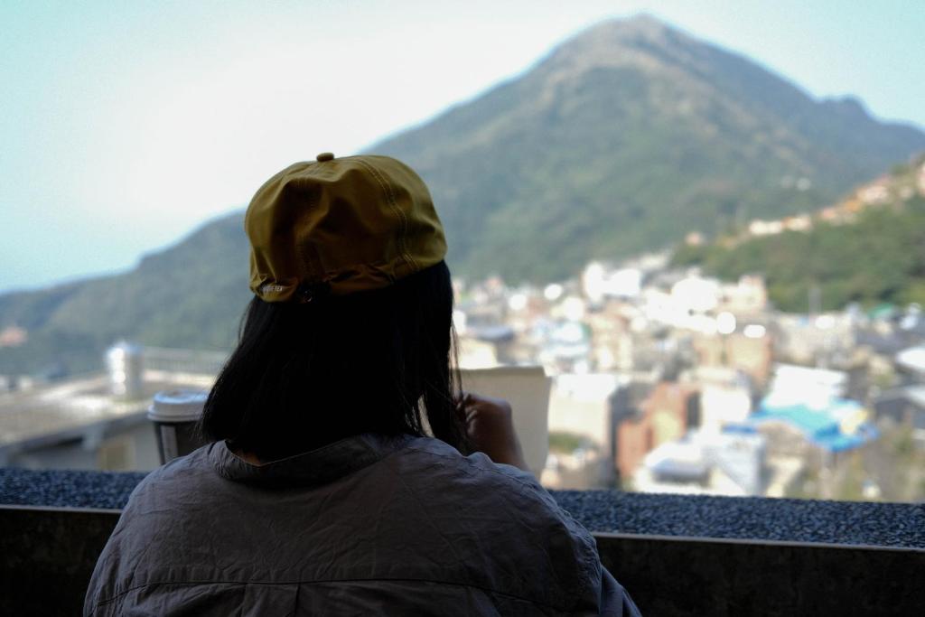 a person sitting on a balcony looking out at a city at Jiufen Breeze 九份惠風民宿ｌ6人包棟小屋 in Jiufen
