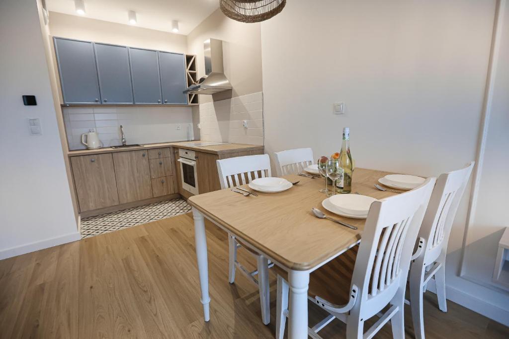 eine Küche mit einem Holztisch und weißen Stühlen in der Unterkunft M&K Apartamenty Morska Fala, Gdańsk - Wyspa Sobieszewska in Danzig