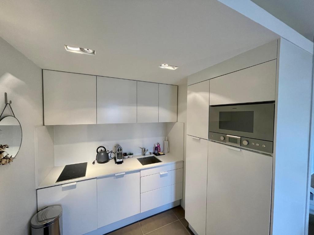 a white kitchen with white cabinets and a refrigerator at Deauville Harmonie - Tout à pied, Balcon &amp; Modernité in Deauville