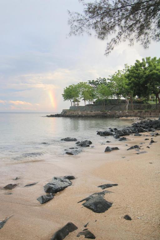 a rainbow in the sky over a beach with rocks at Lombok Sunset Bay Resort in Sekotong