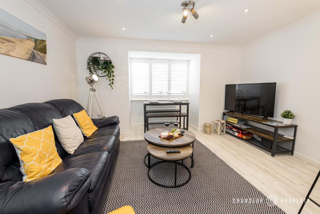 uma sala de estar com um sofá de couro preto e uma televisão de ecrã plano em BMTH town centre 2 min walk, 3 bed house, outside space and parking - Driftwood em Bournemouth