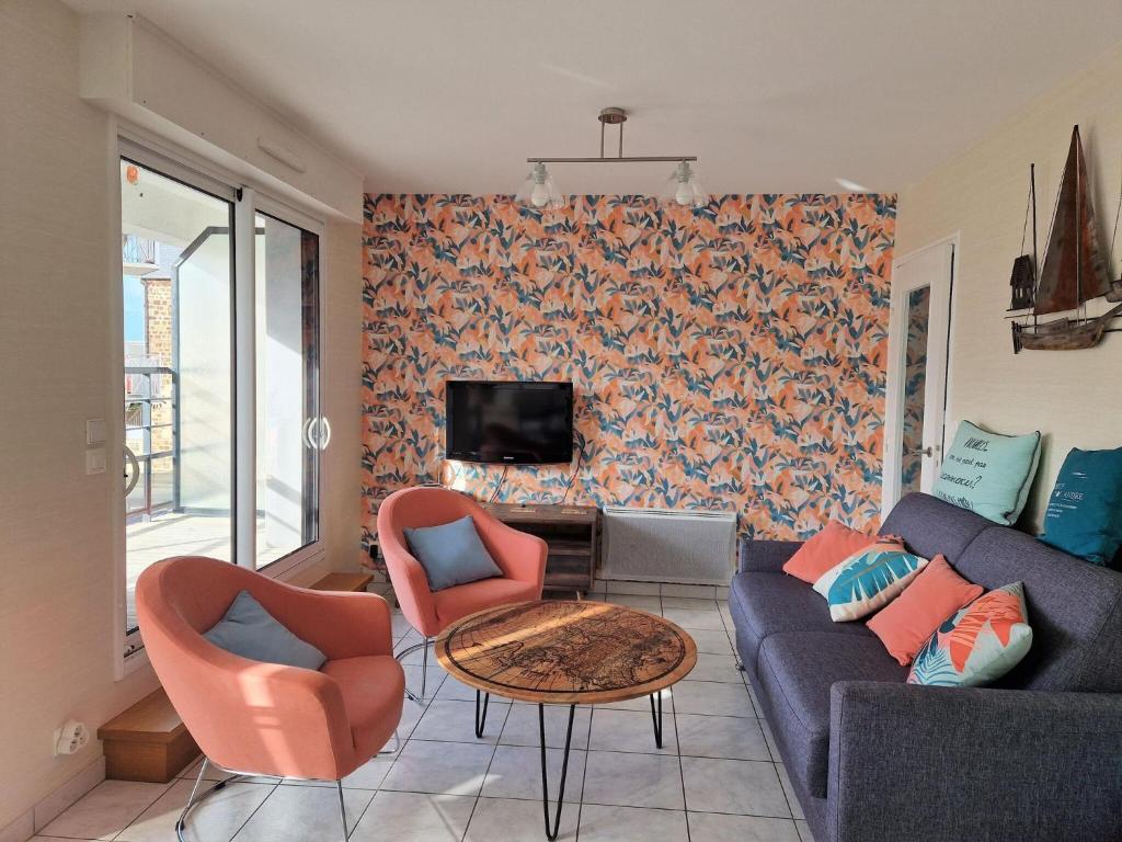 ein Wohnzimmer mit einem Sofa, Stühlen und einem TV in der Unterkunft Nice apartment 50m from the beach with balcony and parking, Pléneuf-Val-André in Pléneuf-Val-André