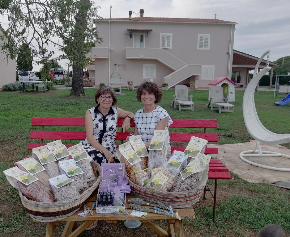 Duas mulheres sentadas numa mesa de piquenique com cestos de comida. em Agriturismo Susanna e Atria em Bibbona