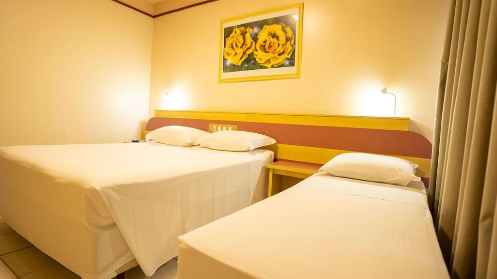 two beds in a room with yellow flowers on the wall at Hamburgo Palace Hotel by Easy Hotéis in Balneário Camboriú