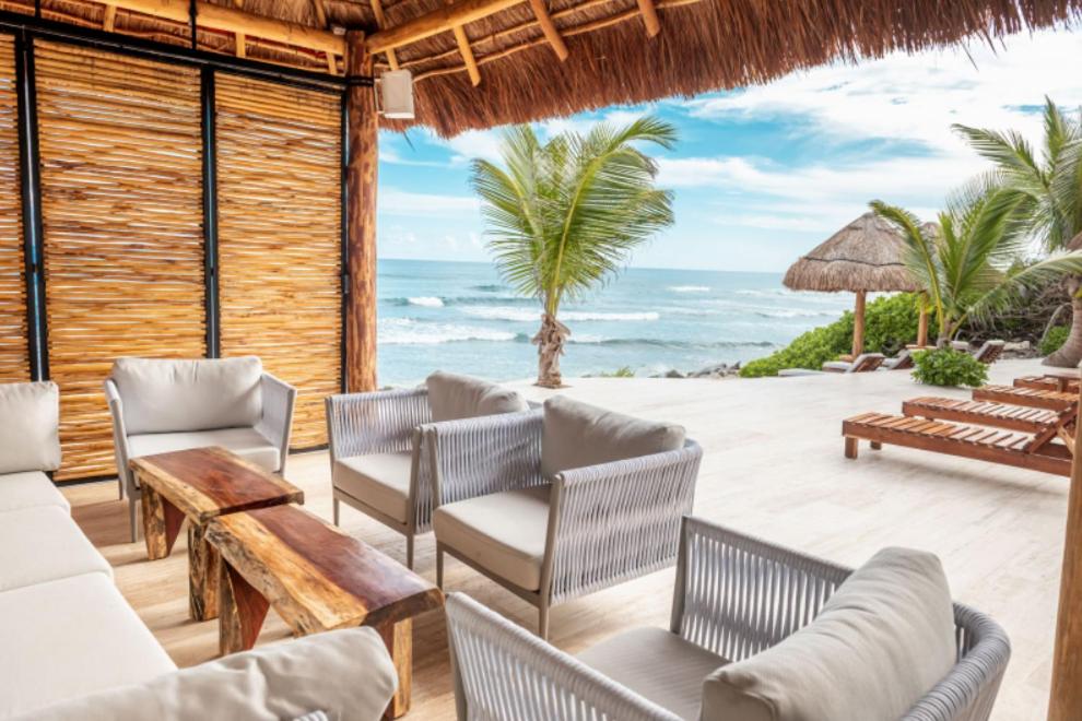 un patio avec des chaises et des tables et l'océan. dans l'établissement Bella Villa, à Tulum