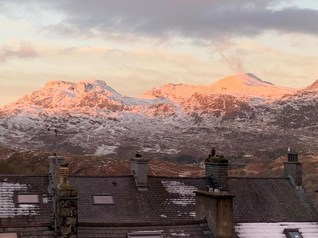 uma vista das montanhas cobertas de neve dos telhados das casas em Cosy cottage in picturesque Snowdonia with stunning views of the Moelwyn mountains em Blaenau-Ffestiniog